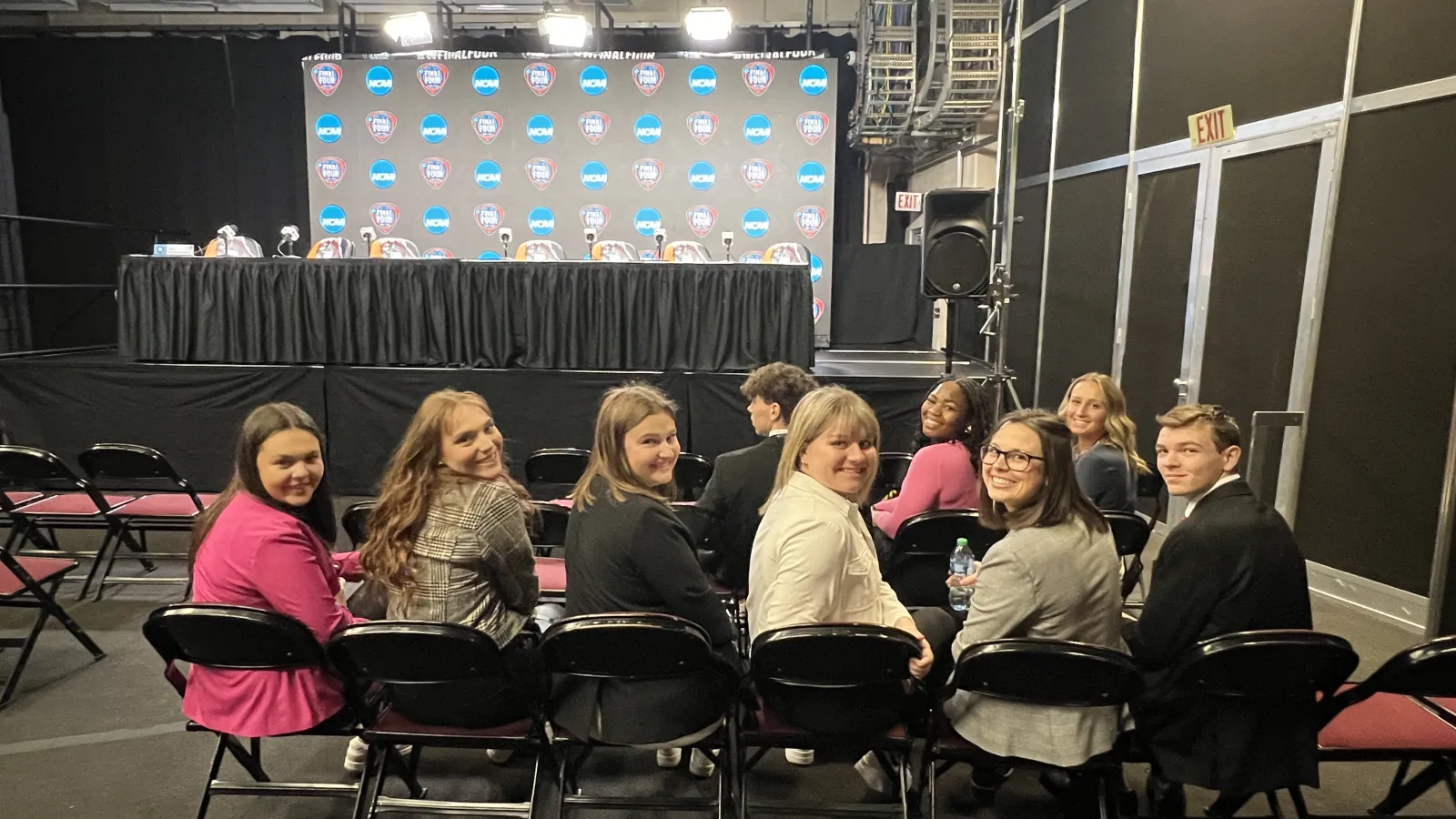 Students sit in chairs with stage and table behind them