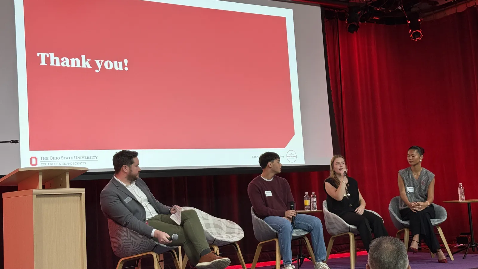 four people on a stage sitting in chairs 
