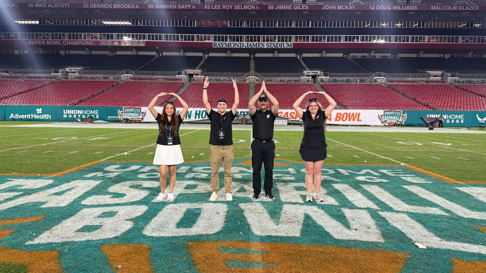 four people doing O-H-I-O on football field